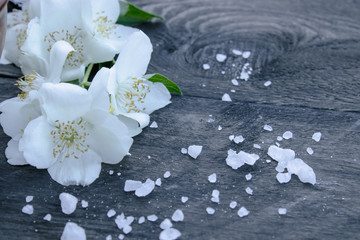 White jasmine flowers and green leaves lie on a wooden background. There is a place for your text.