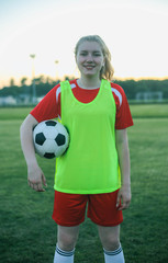 Portrait of a smiling female football player with a soccer ball at sunset