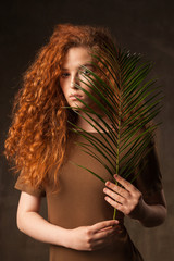 Energizer beautiful young curly ginger hair woman with green tropical plant palm branch posed in...