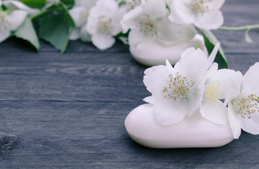 Naklejka na ściany i meble Cosmetic soap and white jasmine flowers with green leaves lie on a wooden background. There is a place for your text.