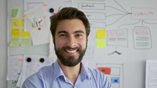Young startup entrepreneur smiling at camera in front of office whiteboard