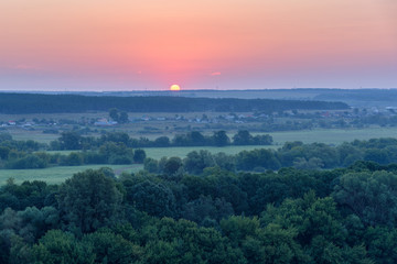 Sun rises in the early morning over the fields and forests