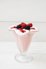 Beautiful pink raspberry snack fruit smoothie or milkshake in a glass with raspberries and blackberries on a white plank . Yogurt cocktail. Natural detoxification. Liquid ice cream.