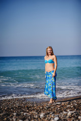 Beautiful young slim girl standing on a sandy beach by the sea. In a blue bathing suit, dress, shawl sarong skirt. Turkey. vacation. Vacation. Sunlight. Place for text. Close up