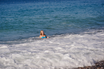 Beautiful young slim girl lying in the water, the beach by the sea. In a blue bathing suit, dress. Turkey. vacation. Vacation. Sunlight. Place for text. Wave covers the woman. Falls from waves.