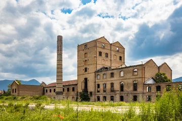 Tafelkleed An old disused factory, abandoned and in ruins, with a smashed roof and a chimney. Tall weeds invade the building. Concept of economic bankruptcy. Cloudy sky. Italy, Foligno, Umbria. © Ragemax
