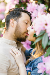 the boy and the girl are kissing in the colors of lilac and pink rhododendron in the spring. tenderness and standing in a relationship