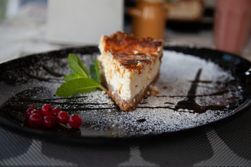 a slice of cottage cheese cheesecake on a large black plate decorated with mint and cranberries