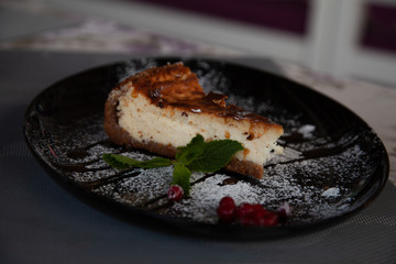 a slice of cottage cheese cheesecake on a large black plate decorated with mint and cranberries