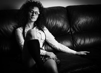 Sensual young sexy girl with curly hair  dressed in student clothes: skirt and shirt , sitting on sofa.  Black and White , Retro (vintage) style. -Picture.