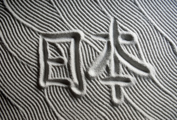 Japanese Zen garden raked with the Chinese characters for Nihon (English translation: Japan) in capital letters in textured white sand