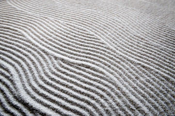 Fototapeta na wymiar Simple graphic wave patterns raked into a background in the white sand of a Japanese Zen garden