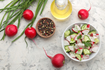 Fresh radish and cucumber salad and greens on a light concrete table. Salad of spring vegetables. ingredients for making salad. top view