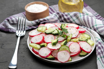 Fresh radish and cucumber salad and greens on a black concrete table. Salad of spring vegetables. ingredients for making salad.