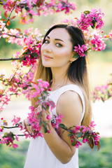 Naklejka premium Beautiful girl with hair color Ombre stands in a blooming pink Apple tree in spring. Beautiful eyes and a pretty face.
