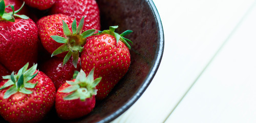 Fresh red strawberries in a ceramic bowl on a wooden white table. fresh fruits. view from above. Copy space for writing.