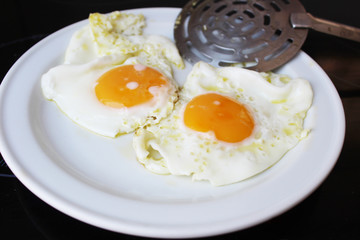 Dos huevos en plato blanco, pala de cocina y fondo negro.