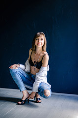Blurred smiling young naked in bra woman fashion look pretty cool model wearing denim blue torn jeans white shirt on black wall studio photoshoot