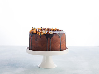 Chocolate drip cake with melting chocolate and peanut for a birthday or celebration on light background with copy space.