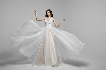 Fototapeta na wymiar Beauty portrait of a young woman in wedding fashion long dress in waving flying fabric, cloth fluttering in wind.