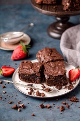 pieces of chocolate nut brownie, on saucer with slices of strawberries, crumbs. Blue, grey...