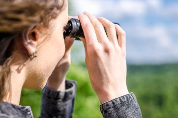A woman with binoculars in her hands looks at the distance in the wild, hunting, looking at a better future.