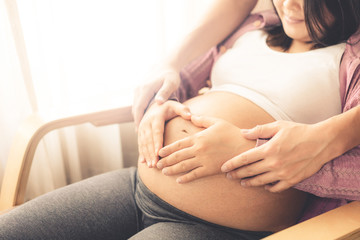 Pregnant couple of husband and wife feels love and relax at home. Young expecting woman holds baby...