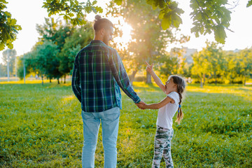 little girl kid daughter holding her father's hand in the background of nature at sunset.