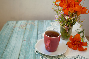 cup of tea on a wooden table with bright orange flowers