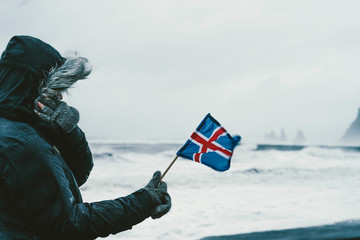 Profile of a man holding a flag from Iceland. Selective focus. Ocean blurred background