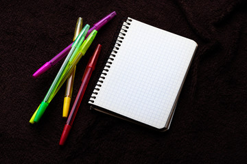 Fototapeta na wymiar notebook and colored pens on black background