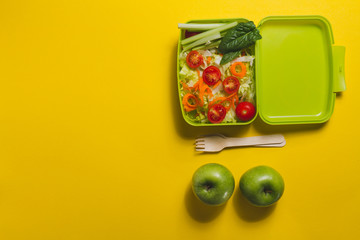 Top view of lunch box with salad and two apples