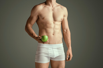 Fototapeta premium Perfect slim toned young body of the man or fit muscular model at studio on grey background. Holding an apple. Concept of sport, diet, healthy lifestyle, bodybuilding, fitness, health care.