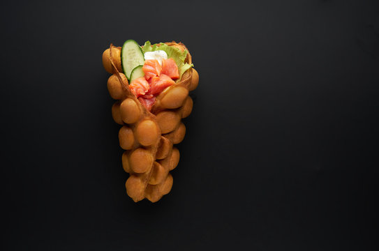 Hong kong or bubble waffle with fresh salmon and sauce on dark bakground. Street food concept
