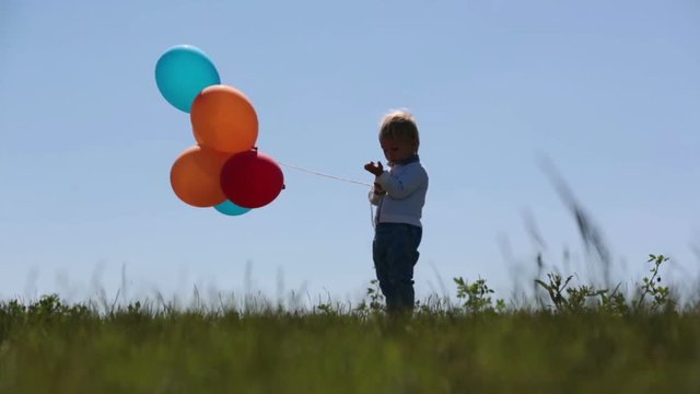 Little boy, toddler, child playing with colorful balloons in the park on kids day, sunny summer afternoon in nature