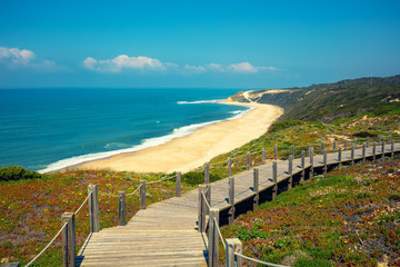 Obraz premium The wooden stairway at the rocky seashore on a sunny day. Polvoeira the beach. Pataias, Portugal, Europe