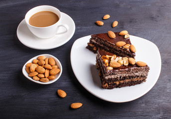 Chocolate cake with caramel, peanuts and almonds on a black wooden background.