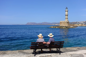 Photo of unidentified elder couple enjoying the view to old Venetian lighthouse in old harbour of Chania, Crete island, Greece