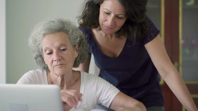 Smiling senior women working with laptop at home. Cheerful mature lady with elderly colleague looking at paper documents and laptop. Business and technology concept