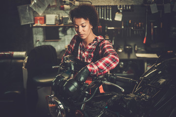 Naklejka na ściany i meble African american woman mechanic repairing a motorcycle in a workshop