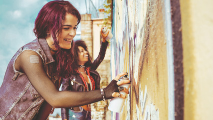 two urban girls painting graffiti on a wall.  Contemporary street culture art and diversity concept.