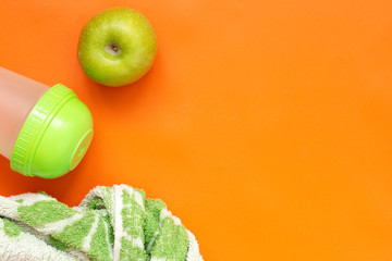 Healthy lifestyle concept, fitness, sport. Green apple, towel and shaker on orange background.
