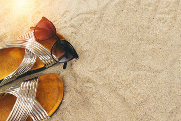 Fototapeta na wymiar Sunglasses and slippers on sand, summer concept 