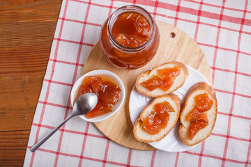 Pear jam in a glass jar on a linen tablecloth on a wooden table.