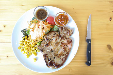 pork chop steak and salad with black pepper sauce and chili sauce on white  dish and wood table with knife