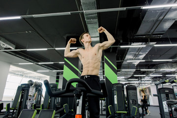 Healthy lifestyle concept. Young sporty man without shirt is exercising bike at spinning class . Cardio training. Young sport man riding stationary bicycle in fitness gym.