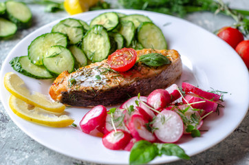 Salmon steak with lemon, tomatoes, cucumber and radish on a plate. Healthy seafood. Proper nutrition food.