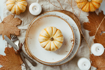 Top view on a decorated table setting for Thanksgiving dinner. Autumn ornate, white pumpkin on ceramic plates.