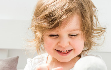 Beautiful smiling blonde baby girl looking down playing close portrait on light background