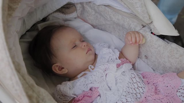Beautiful little girl sleeping in a baby carriage on the street.